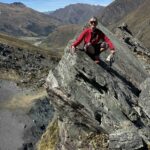 Woman in red jacket on top of rock with big drop below