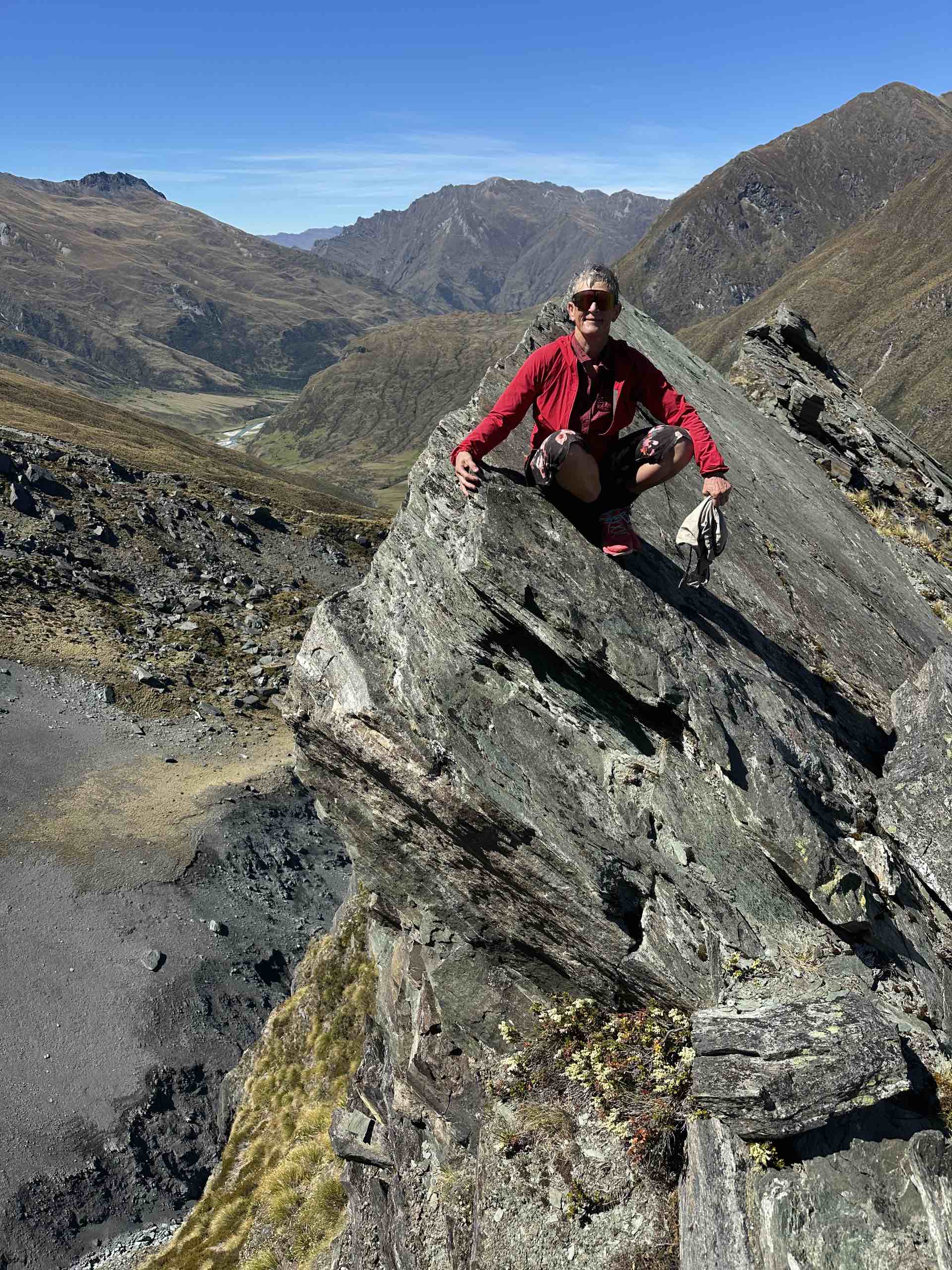 Woman in red jacket on top of rock with big drop below